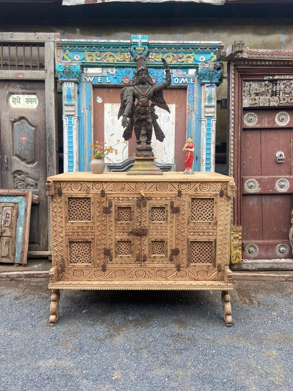Vintage carved wooden dowry chest displayed with a large decorative statue, a small figurine, and a vase on top.