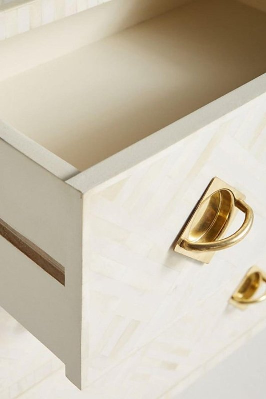 Open drawer close-up of a white optical bone inlay dresser revealing a smooth cream interior, with diamond brass pull hardware and geometric inlay pattern on the drawer front.