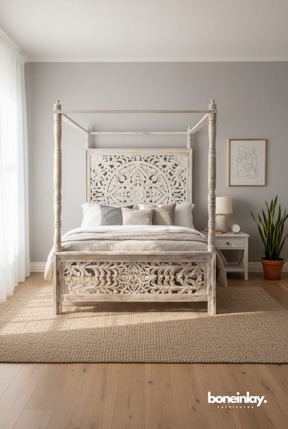 A white, hand-carved solid wood four-poster canopy bed with headboard an elaborate, large-scale circular floral relief carving on the headboard, styled in a bright, modern bedroom.