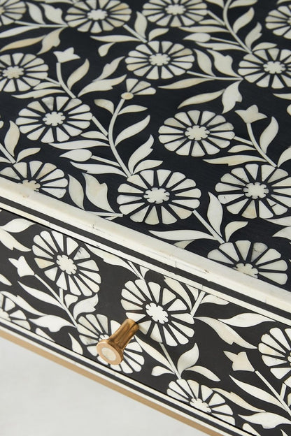 Black floral bone inlay hallway table in a close-up view, highlighting the white inlay pattern across the drawer fronts, the textured decorative surface, a round brass knob, and the detailed face of the three-drawer console table.
