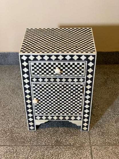 Handmade black and white checkerboard bone inlay bedside cabinet with one drawer and one cabinet door, floral border motif, carved white bone knobs, shot from slight angle showing top surface