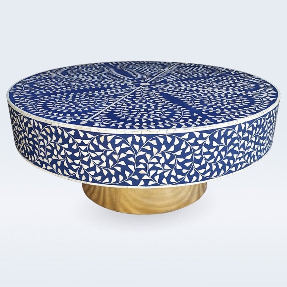 Front angle of a round royal blue and ivory bone inlay coffee table with a floral vine motif across the tabletop and sides, supported by a cylindrical brushed gold pedestal base. The handcrafted piece is shown with the full tabletop and base visible.