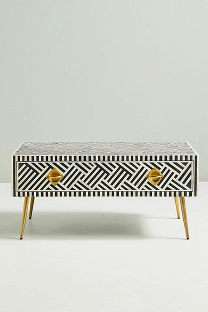 Black bone inlay optical coffee table with brass legs and storage drawer, front angle on plain backdrop