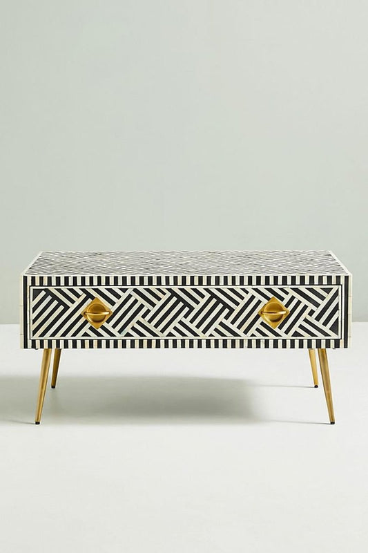 Black bone inlay optical coffee table with brass legs and storage drawer, front angle on plain backdrop