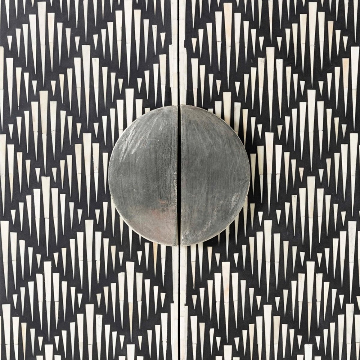 Macro detail of a circular split brushed metal door handle on a bone inlay bar cabinet, surrounded by hand-set ivory spike-shaped bone pieces inlaid on a black resin ground in an Art Deco pattern
