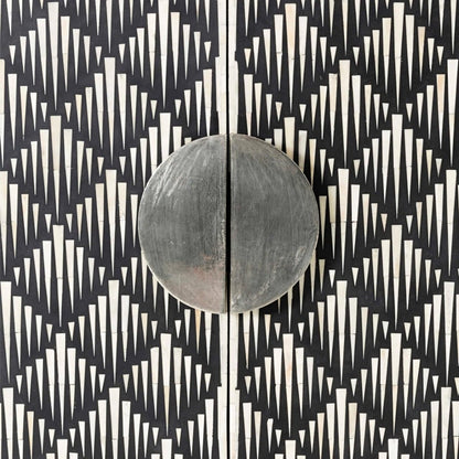 Macro detail of a circular split brushed metal door handle on a bone inlay bar cabinet, surrounded by hand-set ivory spike-shaped bone pieces inlaid on a black resin ground in an Art Deco pattern