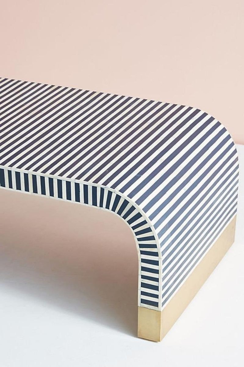 Front right close-up view of a handmade bone inlay waterfall coffee table, showing navy and white diagonal stripes across the tabletop, curved waterfall edge, vertical inlay on the side, and a gold-tone base at the rounded corner.