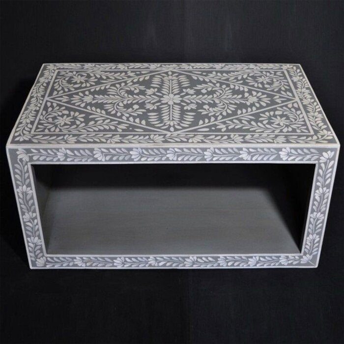 Bone inlay coffee table with white floral and vine pattern on grey background, rectangular waterfall frame with open lower shelf, photographed on dark studio background