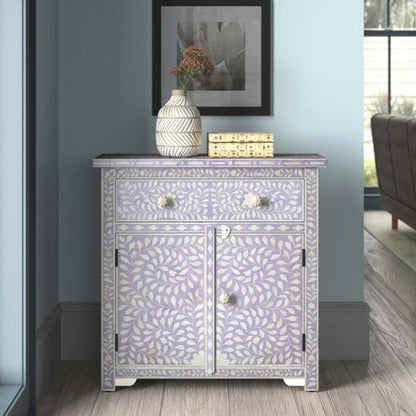 Bone inlay lavender entryway cabinet with white leaf pattern, one drawer and double-door storage, styled with a ceramic vase and decorative box on top against a blue-grey interior wall.