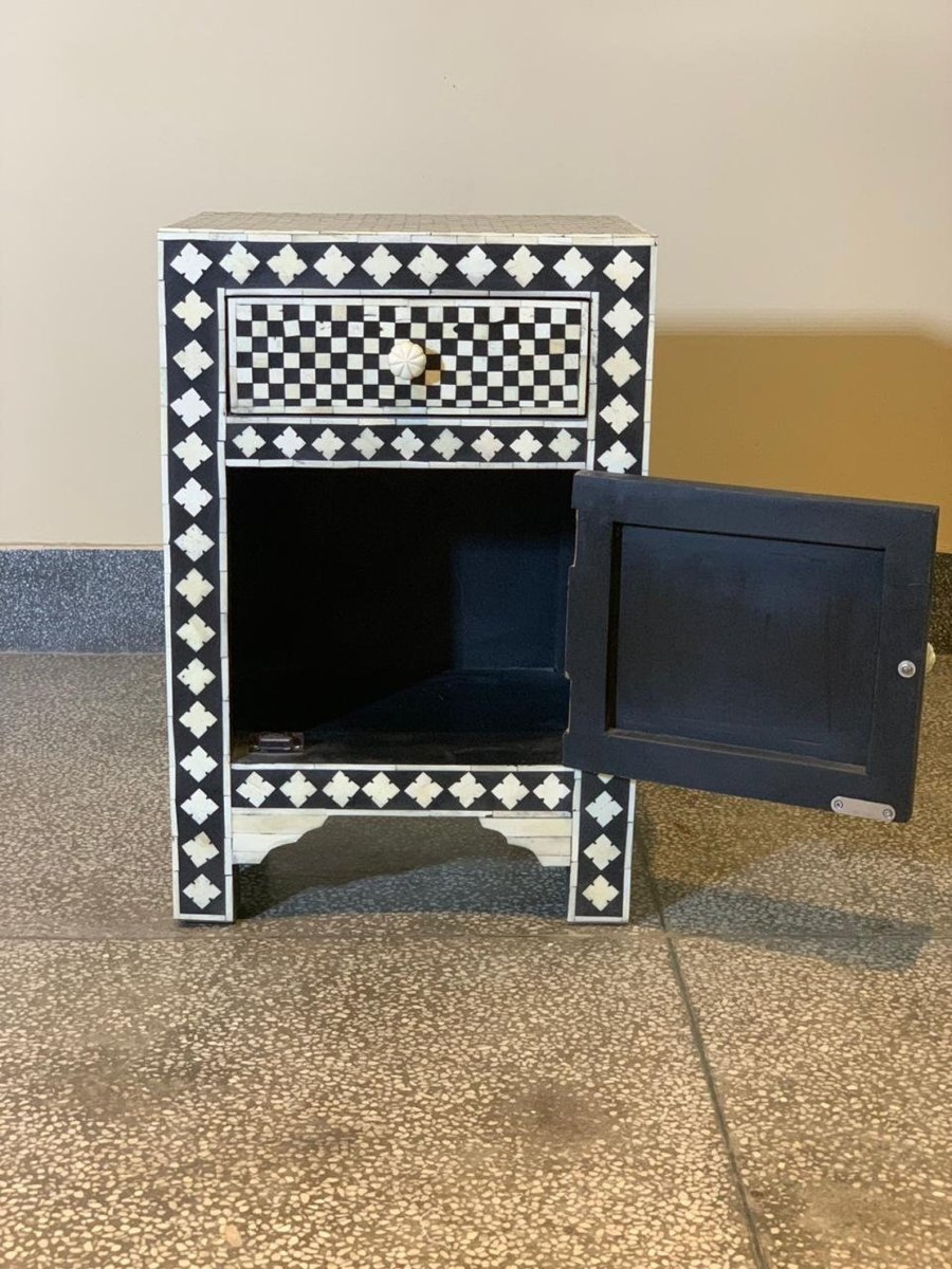 Black and white bone inlay nightstand with cabinet door open revealing interior storage space, checker and diamond pattern inlay on all exterior panels, carved bone knob on drawer, arched wooden base