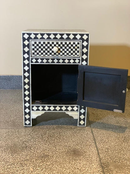 Black and white bone inlay nightstand with cabinet door open revealing interior storage space, checker and diamond pattern inlay on all exterior panels, carved bone knob on drawer, arched wooden base