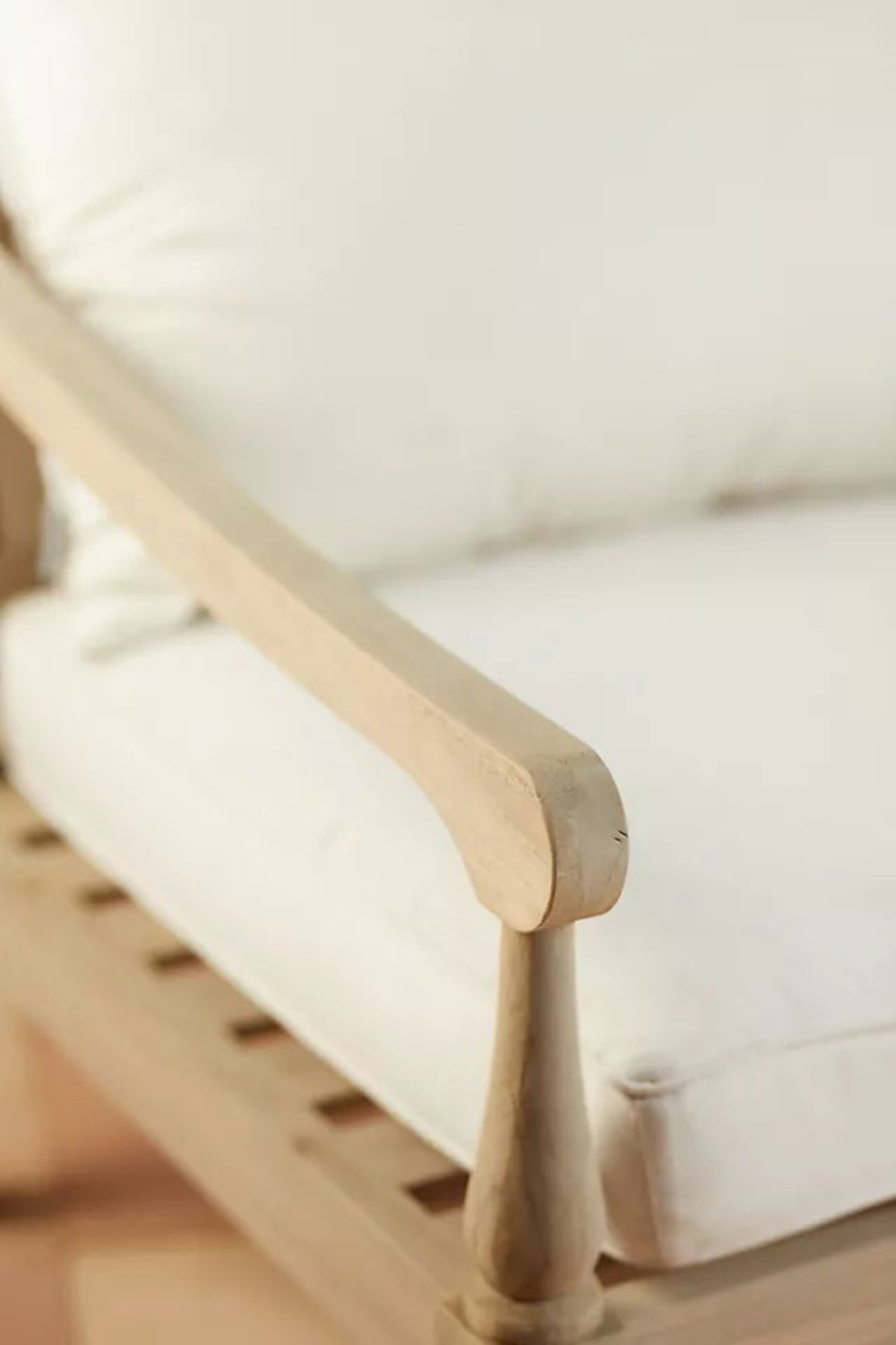 Curved arm lounge bench in solid wood, corner detail view showing the rounded armrest end beside a light seat cushion.
