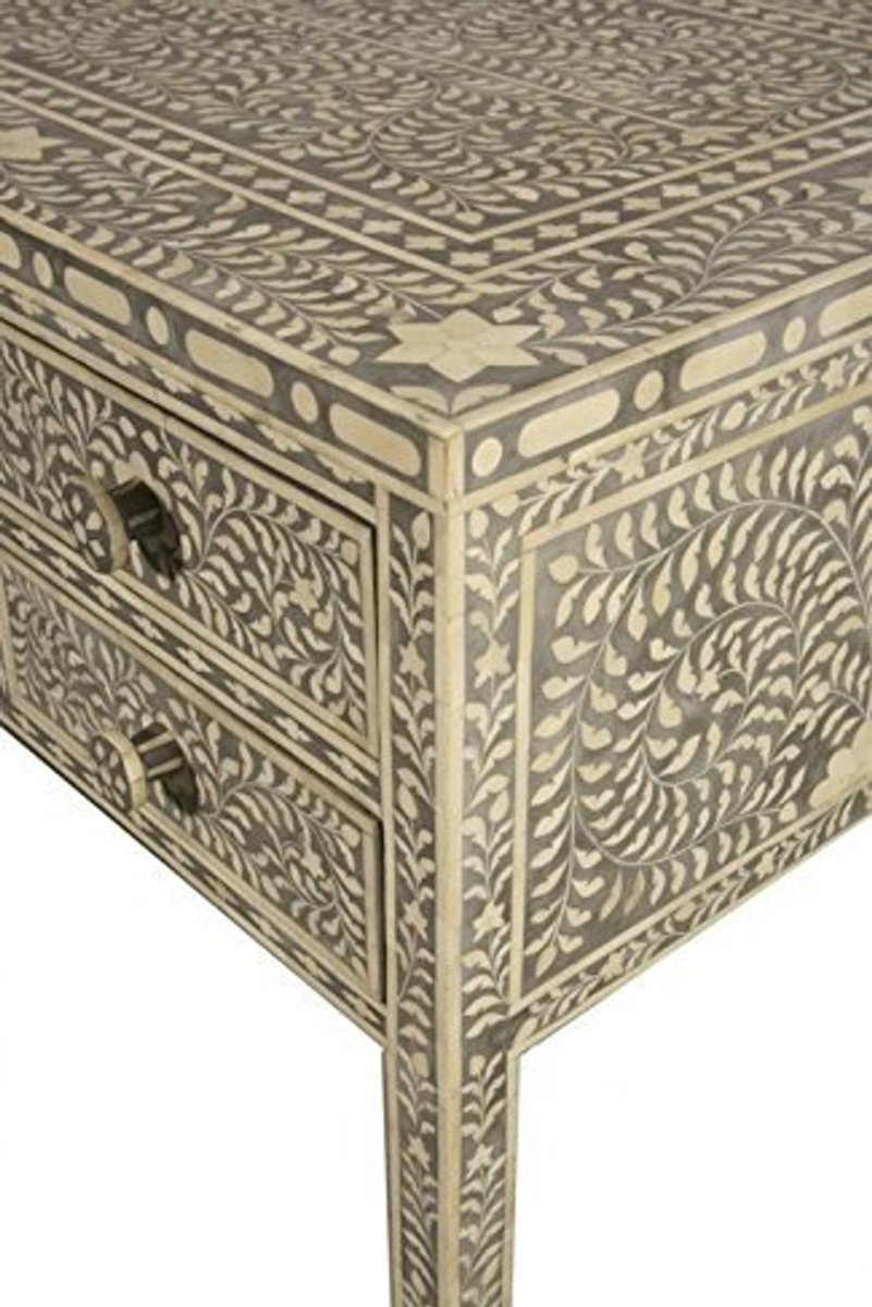 Close-up corner view of a grey and ivory handmade bone inlay vanity desk, showing floral inlay across the top, drawer front, side panel, and tapered leg. This detailed angle reveals the repeating leaf pattern, geometric borders, and drawer hardware.