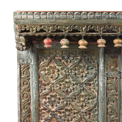 Floral carved wood credenza, corner detail view of the upper left panel, scrolling trim and colorful hanging ornaments.