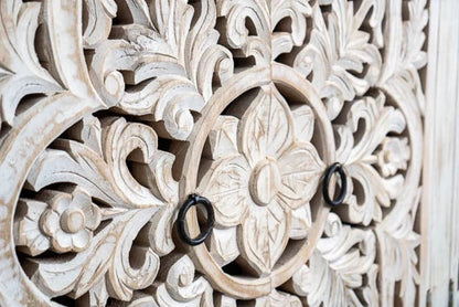 Floral ring-pull storage cabinet in rustic wood, close-up of carved door flowers with two dark circular handles.