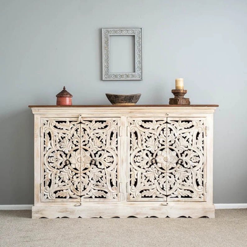 Hand-carved wooden buffet in a rustic finish, front view with floral doors, a bowl and candle beneath a wall frame.
