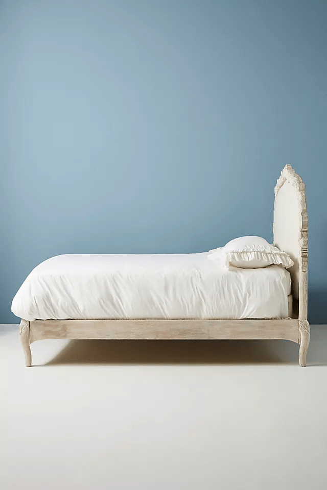 French provincial Menagerie bed in whitewashed mango wood with arched linen headboard,
dressed in crisp white bedding against a soft blue wall,
showcasing carved cabriole legs and low-profile platform silhouette.