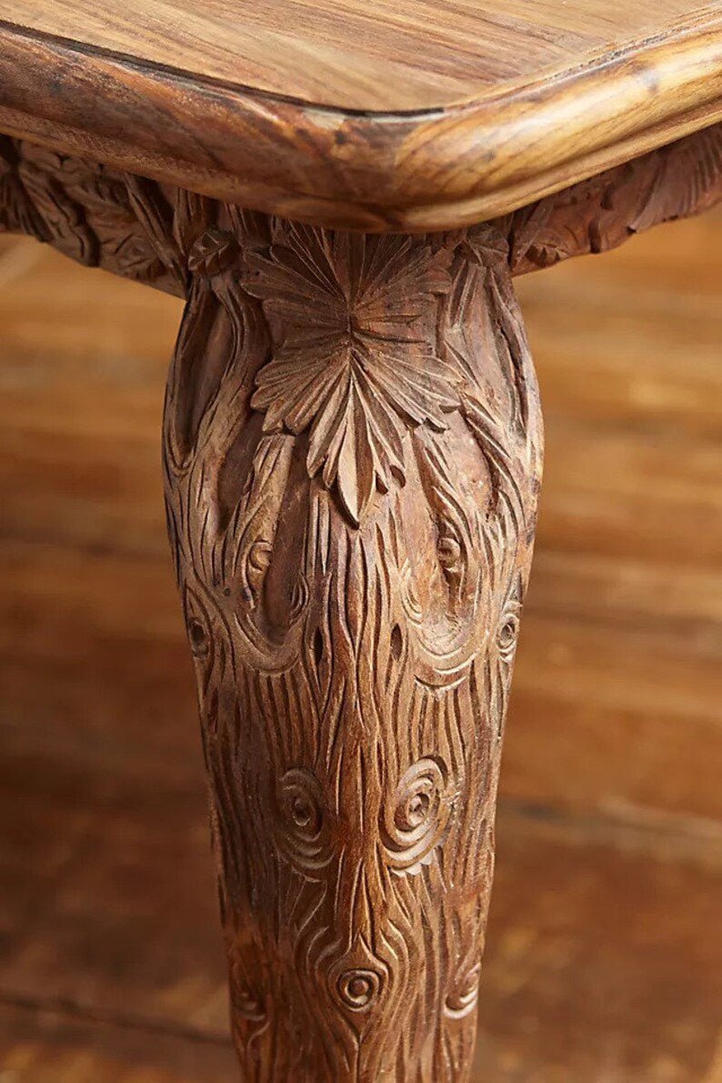 Hand carved wooden dining table in a warm finish, close-up of leg showing raised carving below the top corner.