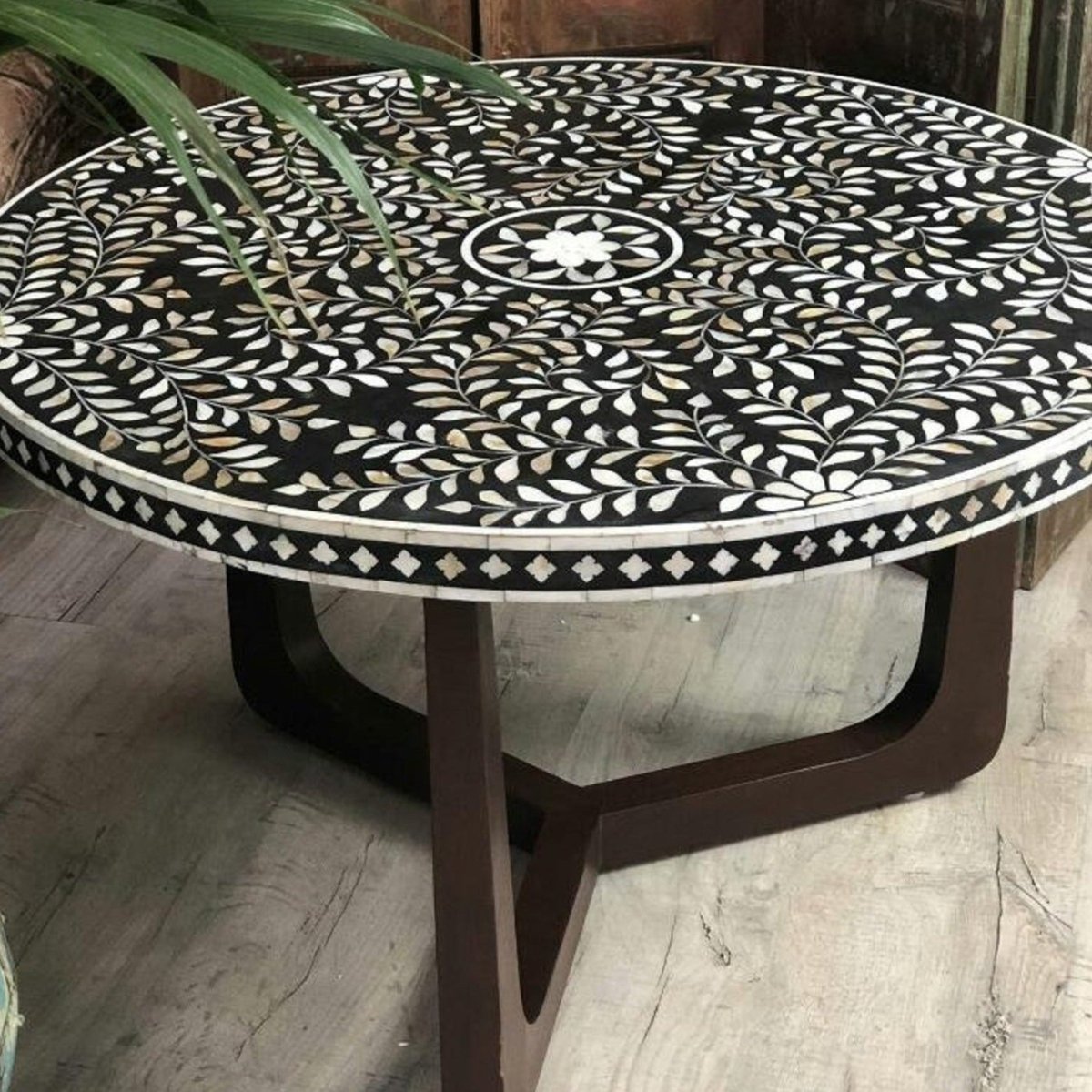 Handcrafted black floral bone inlay round coffee table shown in a front angle, with a black-and-white floral vine pattern across the tabletop and brown legs supporting the rounded solid-wood base for a living room or hallway setting.