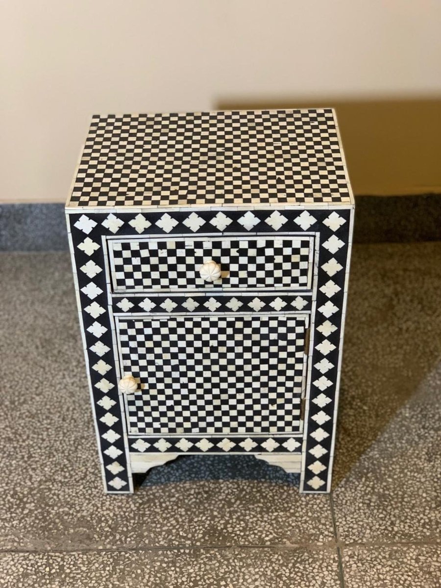Handcrafted bone inlay nightstand in black and white checker pattern with diamond border, one drawer with carved knob, lower cabinet door, angled view showing top and front panels