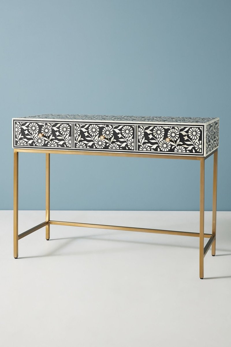 Handcrafted floral bone inlay entryway table in a front angle, showing the complete black console with three drawers, repeated white floral inlay, brass knobs, a slim rectangular top, open space beneath, and a gold-toned metal base.