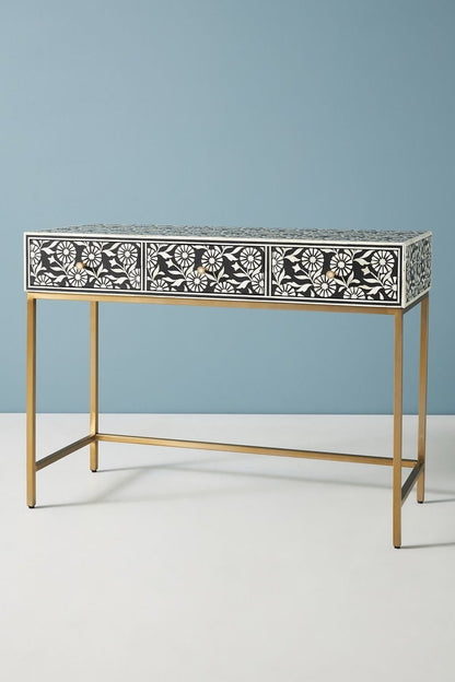 Handcrafted floral bone inlay entryway table in a front angle, showing the complete black console with three drawers, repeated white floral inlay, brass knobs, a slim rectangular top, open space beneath, and a gold-toned metal base.