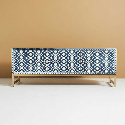 Front angle of a handmade indigo and cream bone inlay entertainment unit, showing the geometric ikat pattern across the cabinet front, three storage sections with solid brass handles, and the long rectangular top supported by a slim brass base.