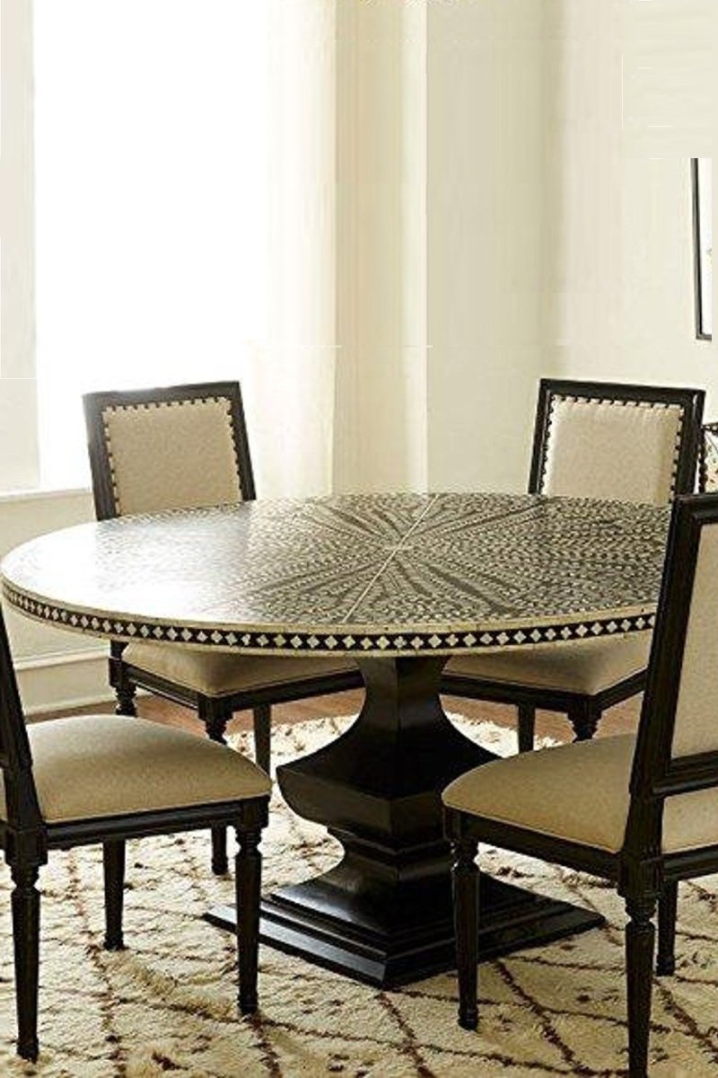 Styled dining room view of a handmade bone inlay floral round dining table shown with dining chairs, featuring the black and white radial tabletop pattern, contrasting checkerboard border, and solid geometric pedestal base.