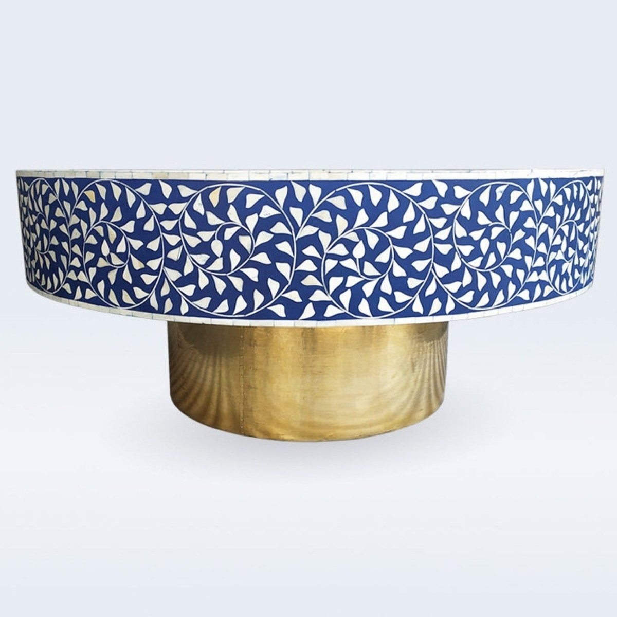 Three-quarter view of a round blue and ivory bone inlay coffee table showing the floral vine inlay across the tabletop, the inlay-covered sides, and the cylindrical brass pedestal base. This handmade accent table presents the complete furniture profile.