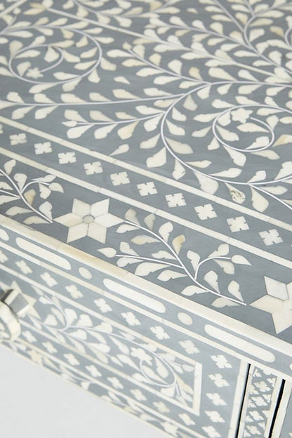 Close-up view of the handmade grey bone inlay coffee table surface, showing the floral inlay motif, contrasting light and grey pieces, and the crafted border detail that defines the tabletop finish. The tight crop focuses on the material and pattern.