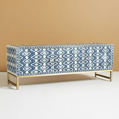 Full front view of a handmade indigo and cream bone inlay media console, showing the repeating ikat pattern across three storage doors, solid brass handles, a straight rectangular top, and the raised brass base against a plain background.