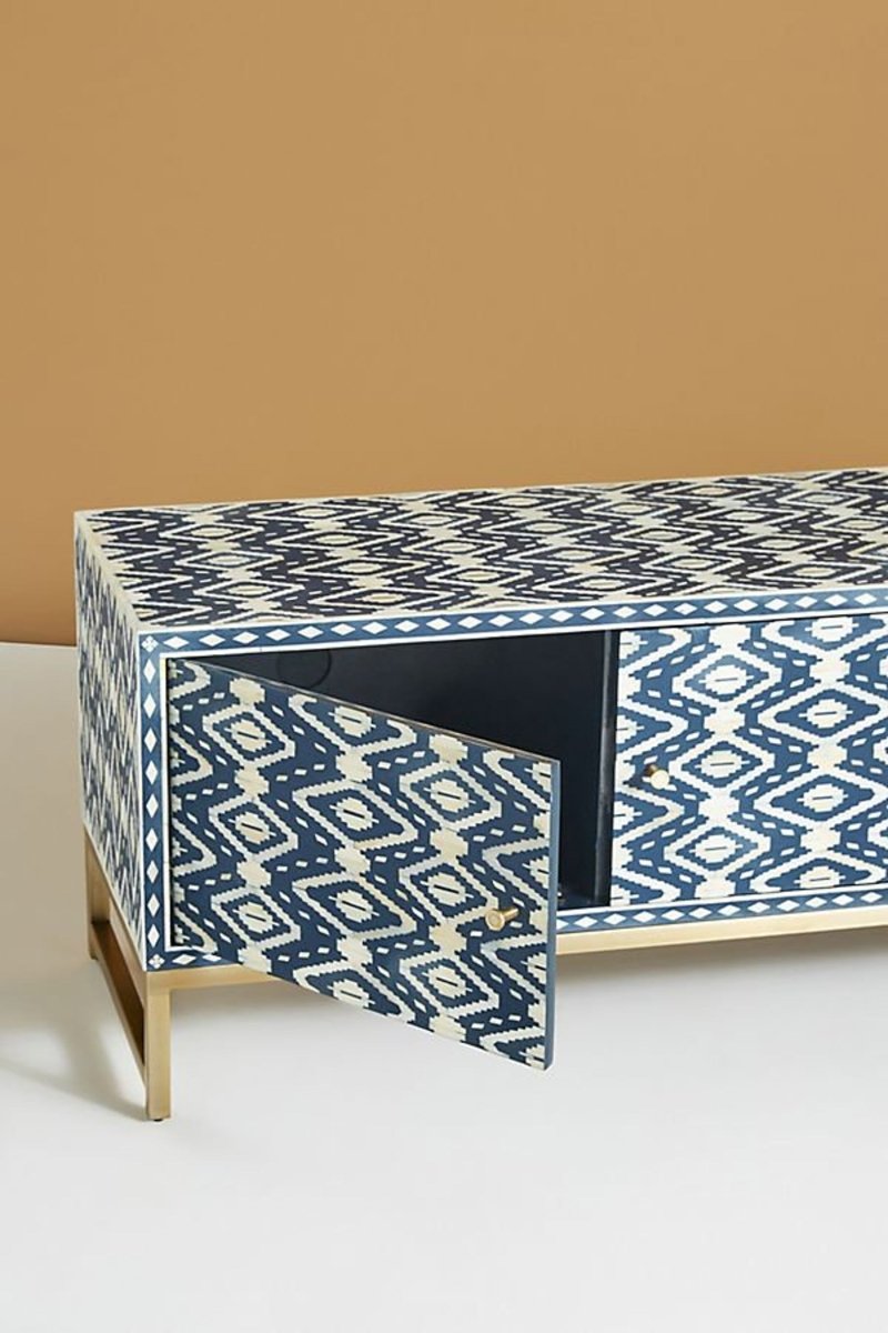Side angle of a handmade indigo and cream bone inlay TV cabinet, showing the cabinet depth, patterned side and front surfaces, three-door storage design, solid brass handles, flat top, and raised brass base against a neutral background.