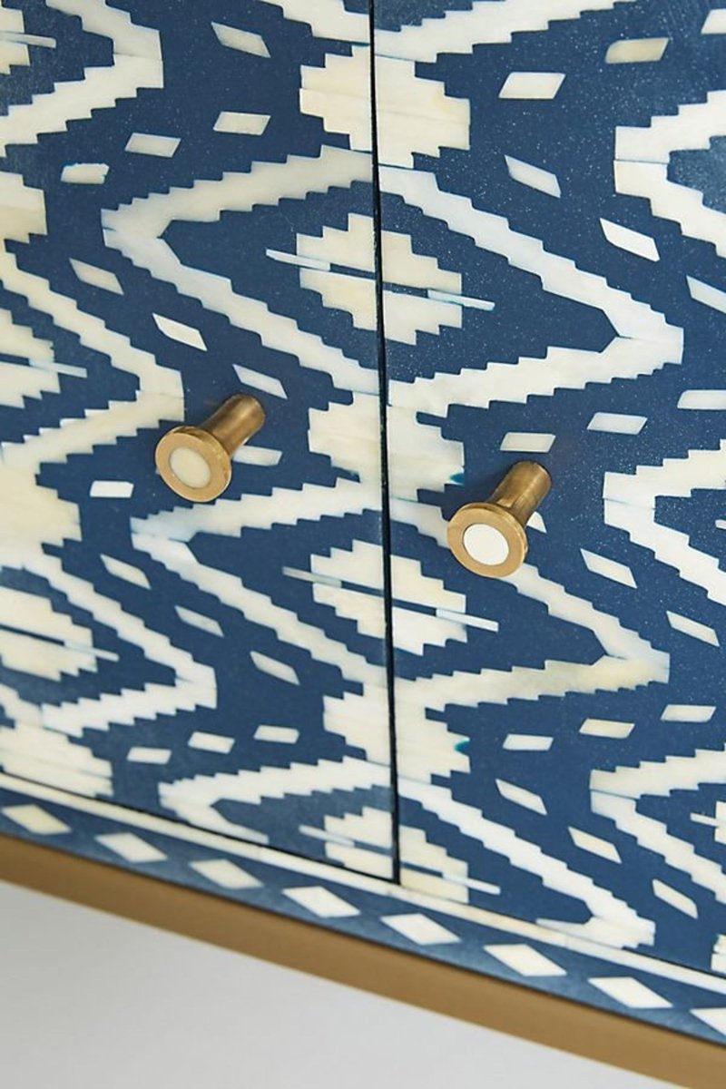 Close-up view of the handmade indigo and cream bone inlay media console, highlighting the individually placed inlay pieces, repeating ikat geometry, smooth cabinet surface, solid brass handle, and precise contrast between the patterned front and brass hardware.