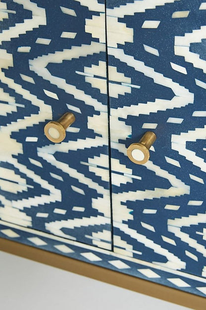 Close-up view of the handmade indigo and cream bone inlay media console, highlighting the individually placed inlay pieces, repeating ikat geometry, smooth cabinet surface, solid brass handle, and precise contrast between the patterned front and brass hardware.
