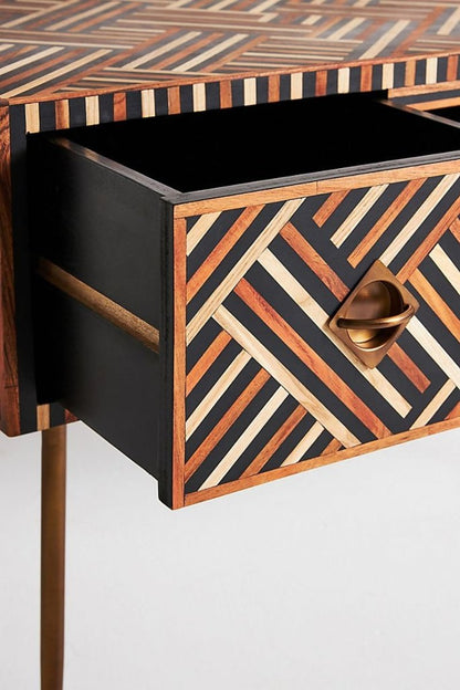 Handmade walnut optical bone inlay laptop desk shown from an angled front side view with one drawer pulled open, revealing its dark interior, brass handle, striped walnut and cream inlay on the drawer front, side panel, and desktop edge.