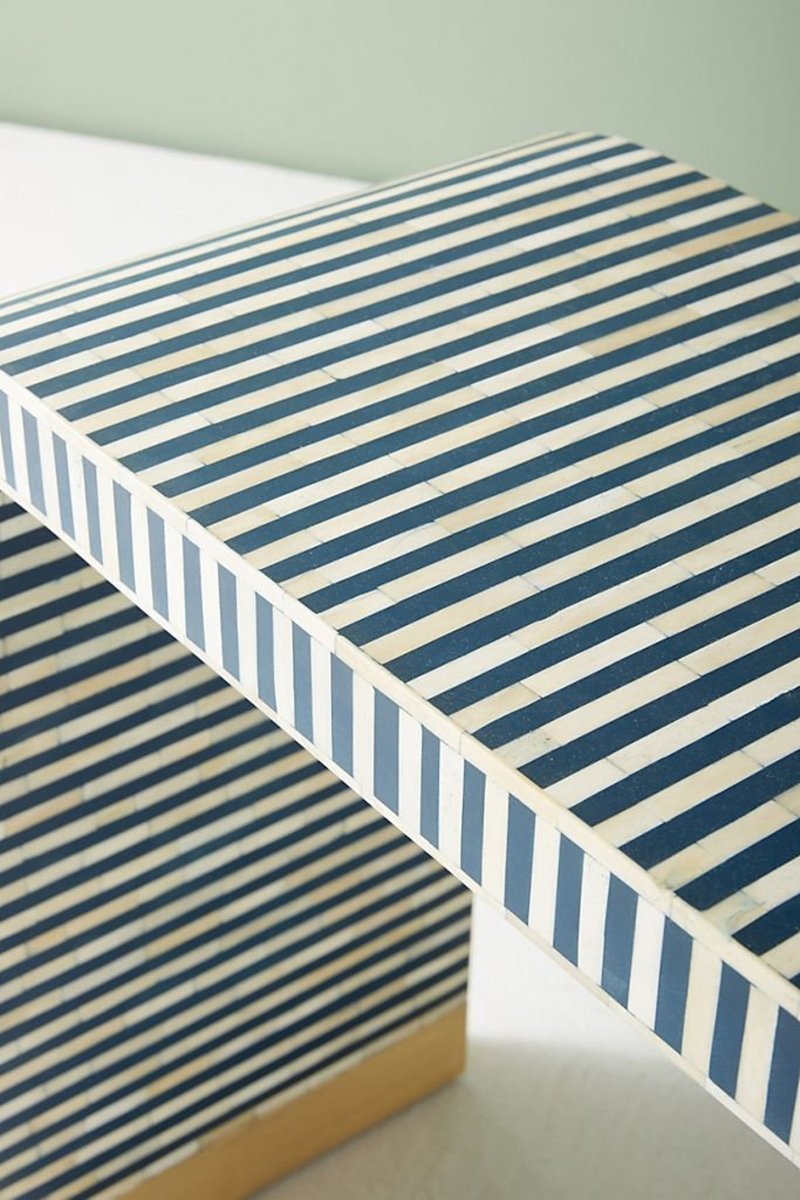 Top and side close-up view of the bone inlay coffee table, highlighting the navy and white striped tabletop, pale inlay border, vertical striped edge, rounded waterfall corner, and a gold-tone base visible beneath the curved side.