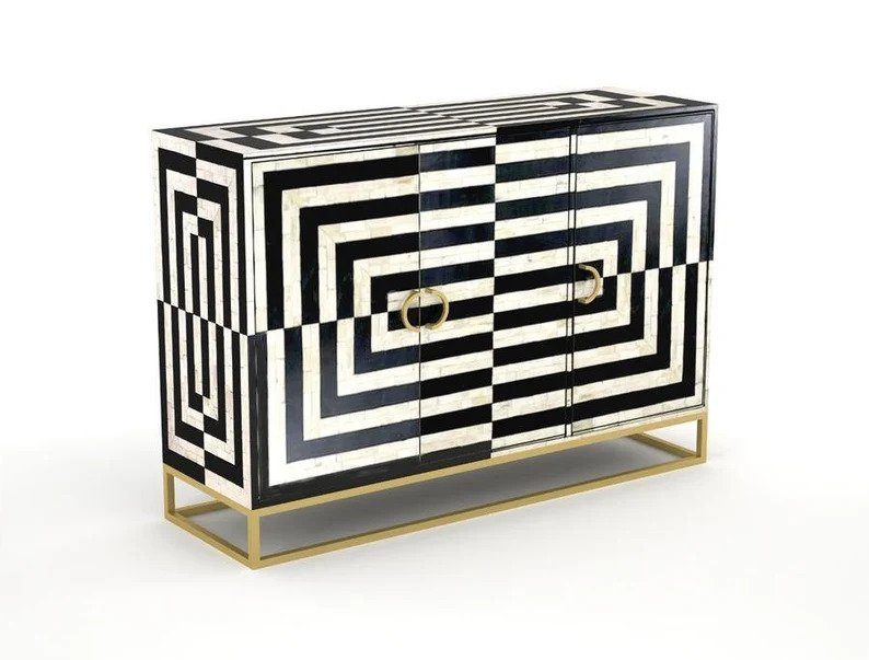 Monochrome bone inlay sideboard featuring concentric geometric optical illusion pattern and brass ring pulls on a gold metal frame, angled product shot
