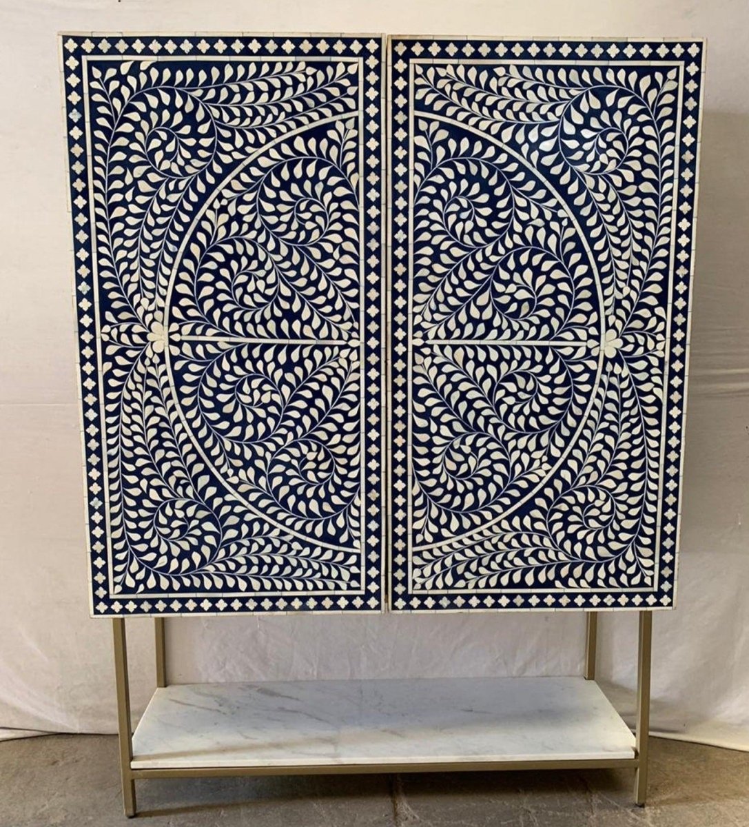 Handmade Bone Inlay Navy Blue Home Bar Cabinet in angled front view, showing floral doors, gold base, and marble shelf