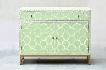 Sage green and white bone inlay cabinet with scalloped shell pattern, one top drawer, two doors, and a gold-finished metal frame on a plain background