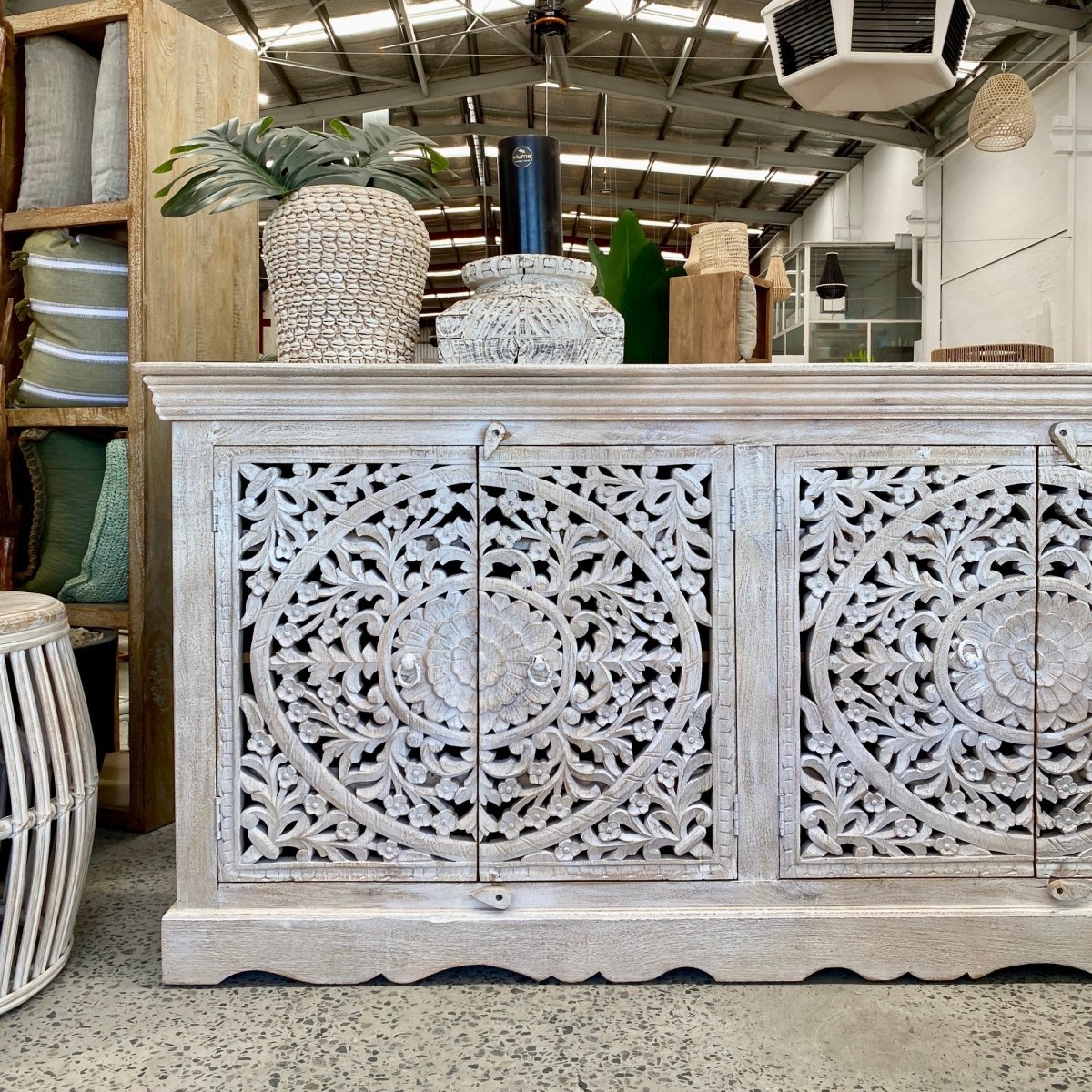 Scalloped base storage cabinet in rustic wood, cropped front view showing floral door carvings beneath decorative pots.
