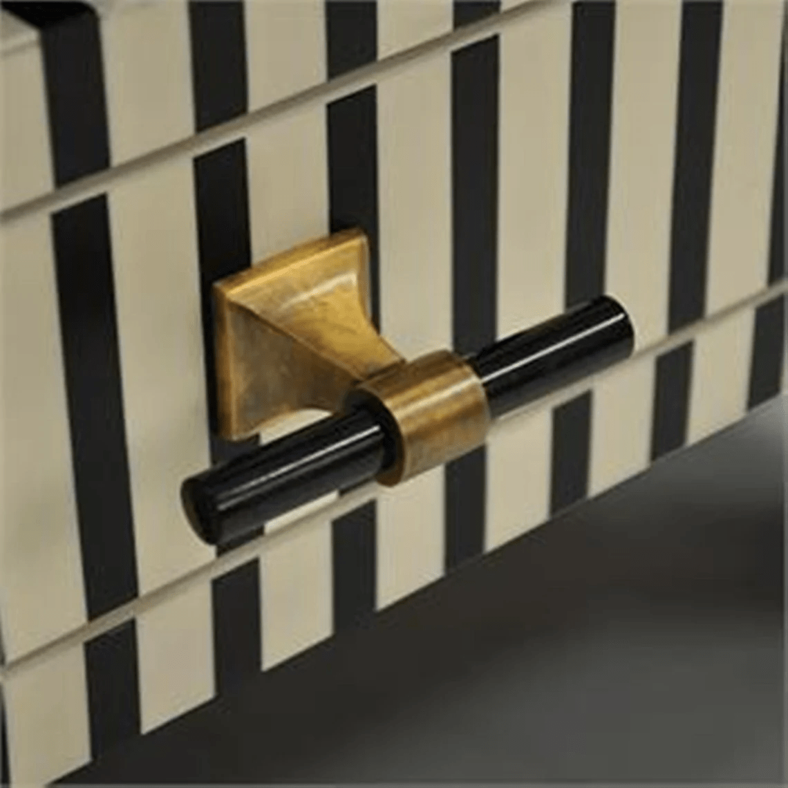 Close detail of a two-tone drawer pull with a brass base and black cylindrical bar on a black and white striped bone inlay nightstand drawer front