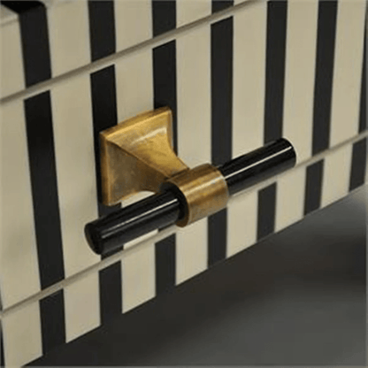 Close detail of a two-tone drawer pull with a brass base and black cylindrical bar on a black and white striped bone inlay nightstand drawer front