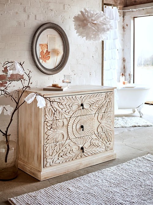 A 3-drawer solid wood dresser with intricate hand-carved floral and leaf patterns in a natural wood finish, featuring black teardrop pulls.