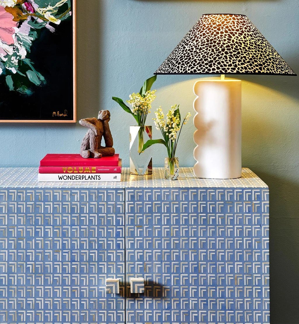 Blue-grey Art Deco bone inlay storage cabinet with repeating geometric tile inlay pattern, styled with lamp, books, and floral arrangement