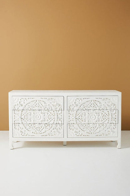 A 6-drawer solid wood dresser in a matte white finish featuring large hand-carved circular floral mandala motifs on the drawer fronts.