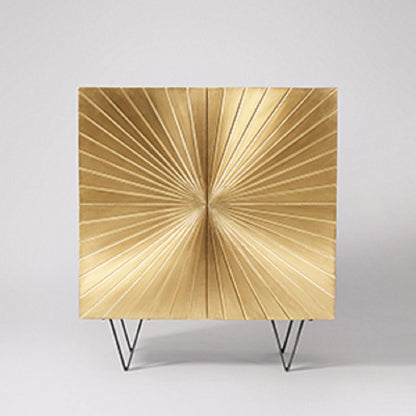 Ziggy two-door square bar cabinet wrapped in a brushed brass gold finish with a large central sculpted sunburst pattern on black metal hairpin legs.
