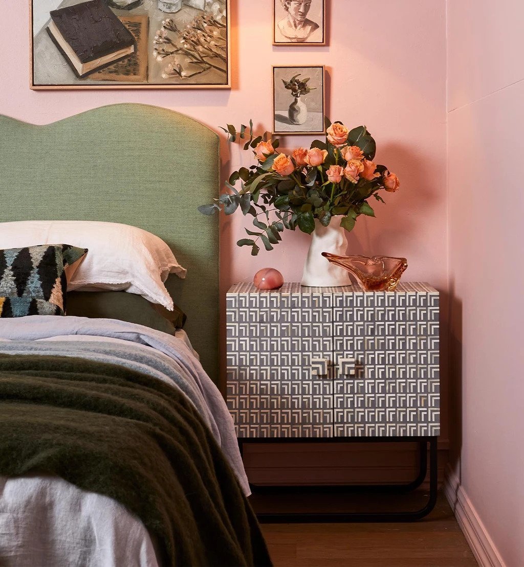 Bone inlay Orleans design nightstand with geometric pattern styled beside a green upholstered bed in a pink bedroom with orange roses