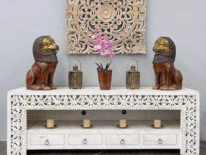 Artisanal white-washed solid wood credenza featuring intricate hand-carved floral patterns, four drawers, and open shelving in a curated living space.
