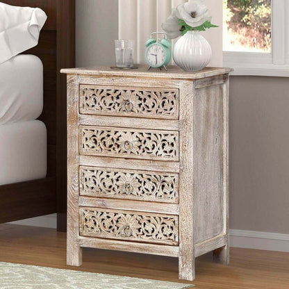Handcrafted four-drawer nightstand in a white-washed finish, featuring intricate, hand-chiseled floral filigree patterns on each drawer front in a rustic bedroom setting.