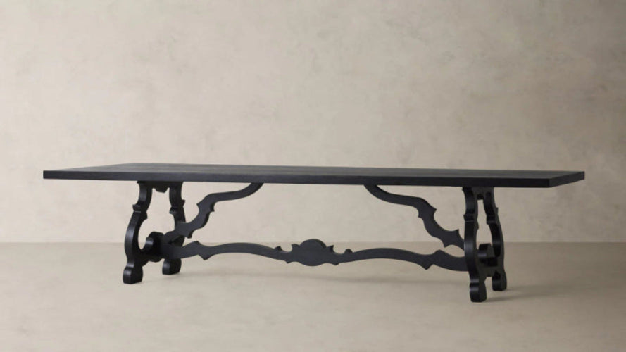 Large matte black solid wood dining table featuring dramatic hand-carved scroll pedestal legs and a traditional Baroque trestle base.